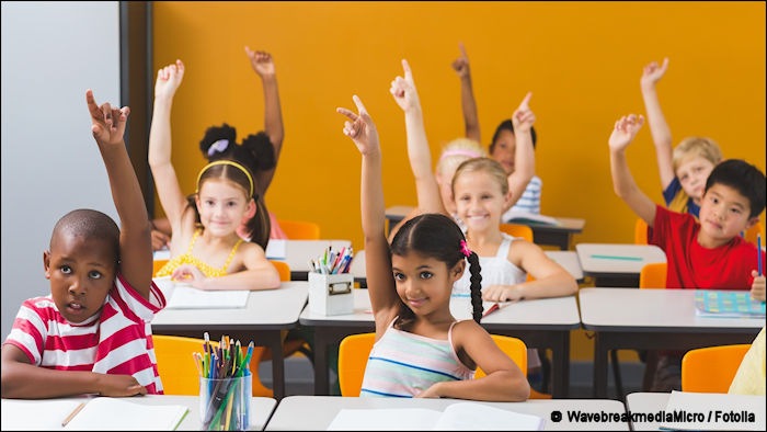  School kids raising hands in classroom